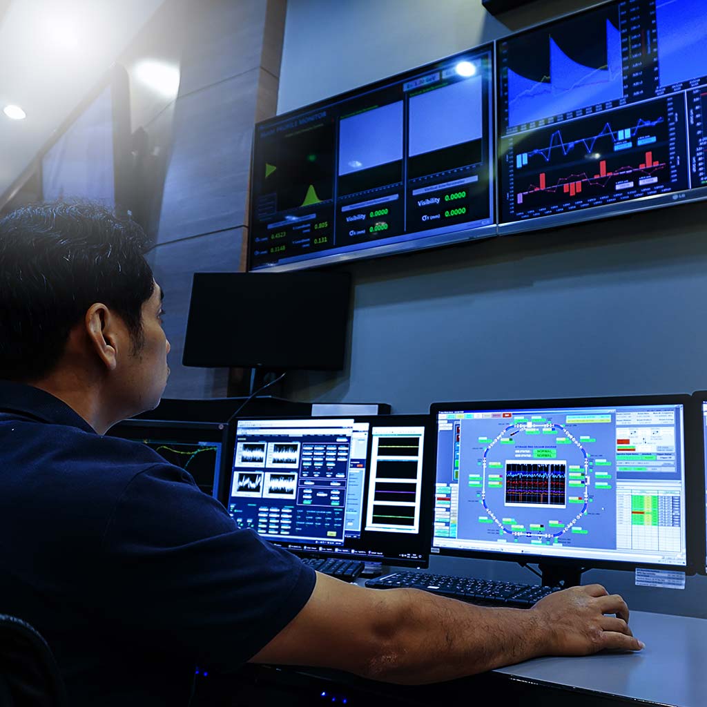 utilities plant engineer at control room desk looking at monitors, with video wall above